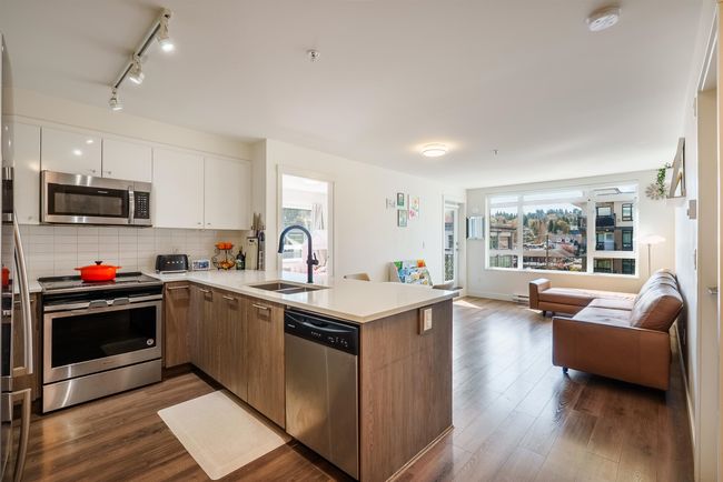 Kitchen featuring stainless steel appliances, open floor plan, a peninsula, light countertops, and dark wood finished floors | Image 7
