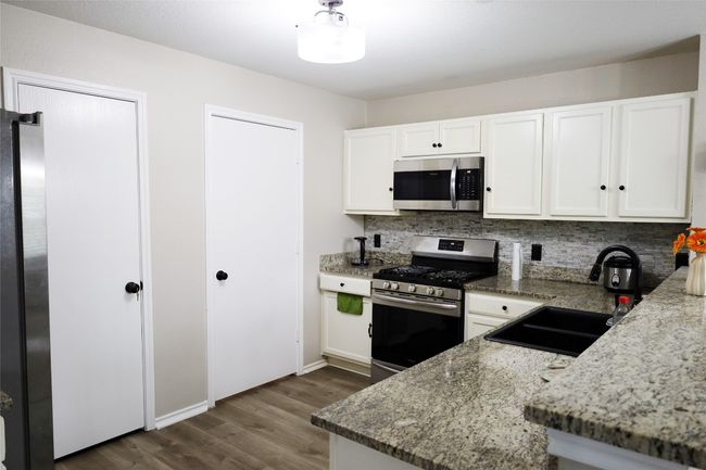 Kitchen featuring white cabinetry, dark wood-style flooring, stainless steel appliances, decorative backsplash, and a sink | Image 6