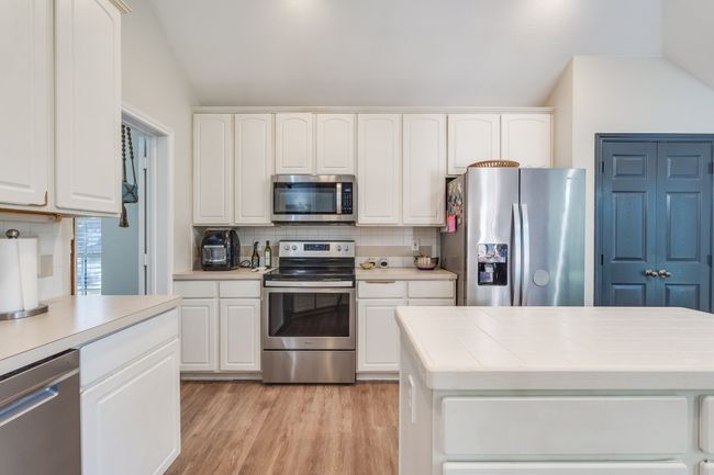 Kitchen featuring stainless steel appliances, tile counters, decorative backsplash, white cabinets, and vaulted ceiling | Image 19