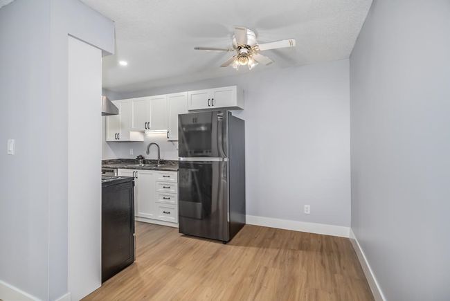 Kitchen featuring freestanding refrigerator, a sink, wall chimney range hood, ceiling fan, and dark countertops | Image 9