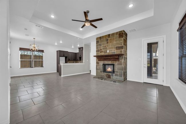 Unfurnished living room featuring ceiling fan with notable chandelier, a fireplace, a raised ceiling, and dark tile patterned floors | Image 8