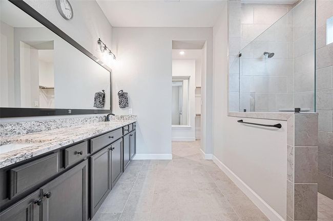 This spa-inspired primary bathroom features a sleek double vanity with granite countertops, framed mirror, and elegant lighting | Image 22