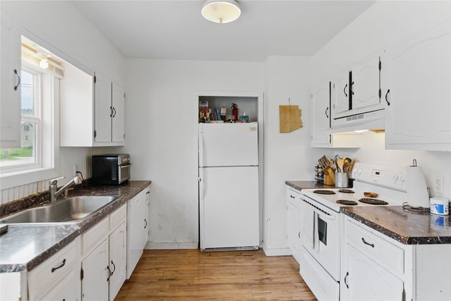 Kitchen featuring light wood-style flooring, a sink, dark countertops, white appliances, and under cabinet range hood | Image 14