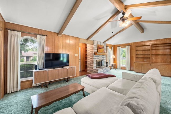 Carpeted living area with wooden walls, ceiling fan, a large fireplace, and built in shelves | Image 10