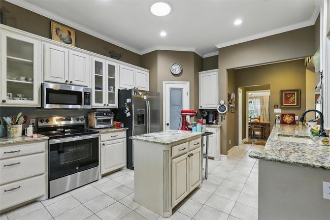 Kitchen with appliances with stainless steel finishes, light tile patterned floors, white cabinets, ornamental molding, and glass insert cabinets | Image 12