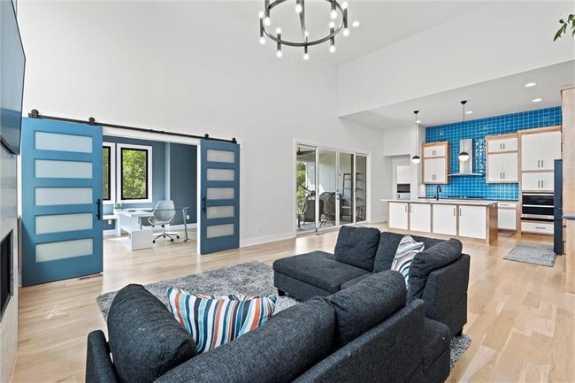 Living room featuring a barn door, a chandelier, a high ceiling, light wood-style floors, and an office area | Image 6
