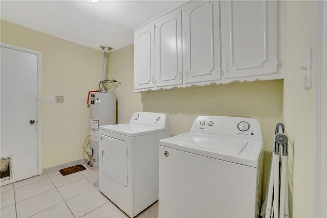 Washroom featuring gas water heater, separate washer and dryer, cabinet space, and light tile patterned floors | Image 25