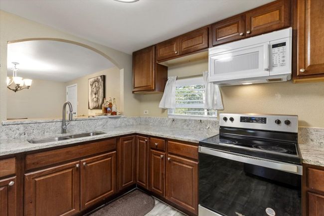 Kitchen with electric range, arched walkways, white microwave, light stone counters, and a sink | Image 9