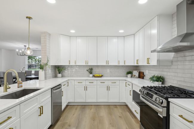 Kitchen featuring a sink, light wood finished floors, white cabinetry, wall chimney exhaust hood, and stainless steel appliances | Image 6