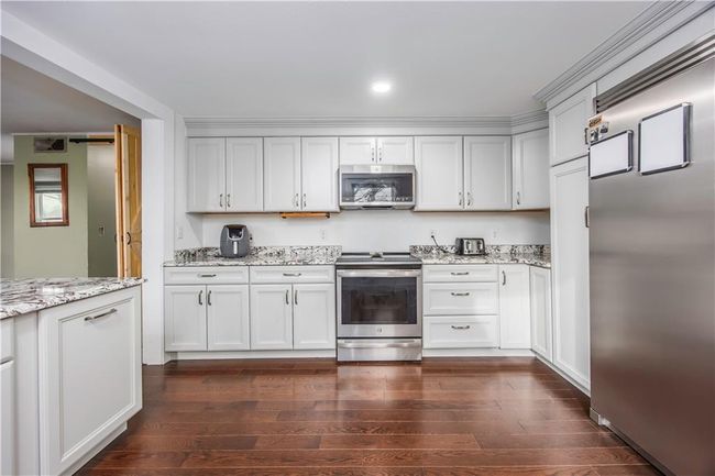 Kitchen featuring white cabinets, stainless steel appliances, dark wood-type flooring, and light stone countertops | Image 35