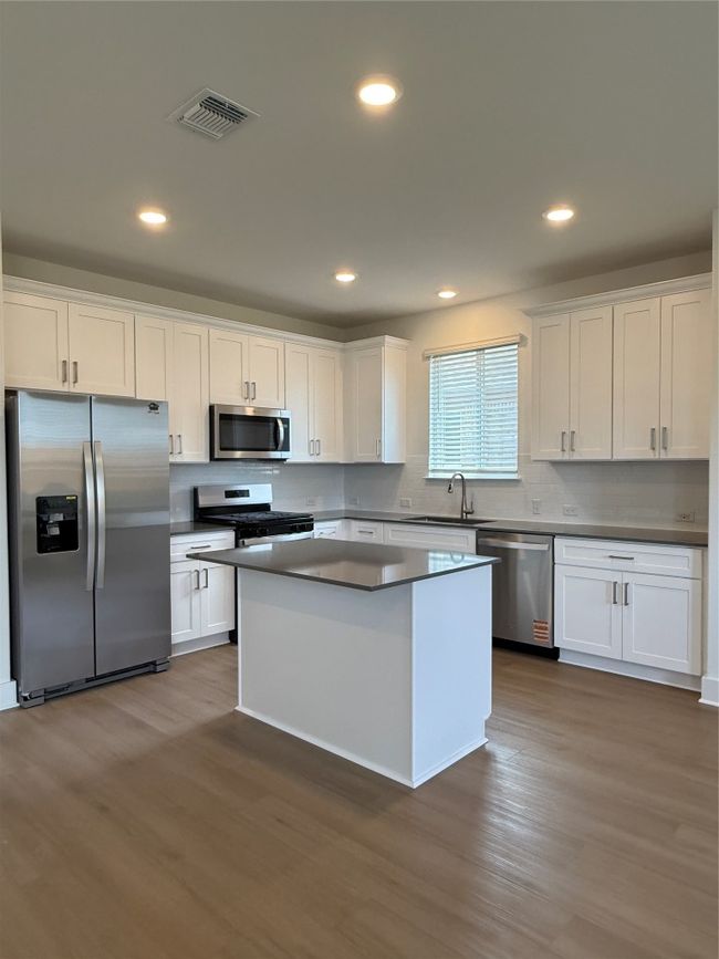 Kitchen with refrigerator, dishwashing machine, a sink, range, and white cabinets | Image 14