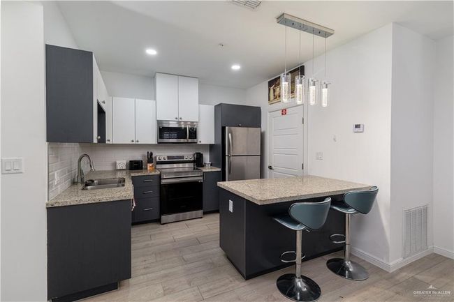 Kitchen with decorative backsplash, visible vents, appliances with stainless steel finishes, light wood-type flooring, and a sink | Image 5