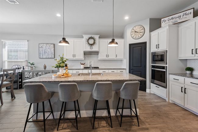 Kitchen with stainless steel appliances, a breakfast bar, white cabinetry, and an island with sink | Image 13
