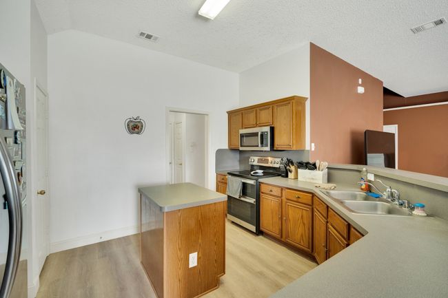 Kitchen featuring stainless steel appliances, light wood-style flooring, a kitchen island, brown cabinets, and a textured ceiling | Image 13