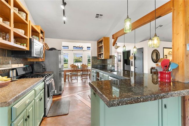 Kitchen with green cabinetry, stainless steel appliances, open shelves, and a sink | Image 10