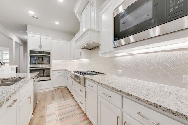 Kitchen featuring decorative backsplash, appliances with stainless steel finishes, a sink, white cabinetry, and visible vents | Image 12