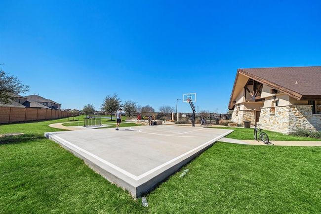 This photo showcases a community recreational area featuring a basketball court, lush green grass, and a nearby building with stone accents. Ideal for outdoor activities and sports enthusiasts. | Image 26