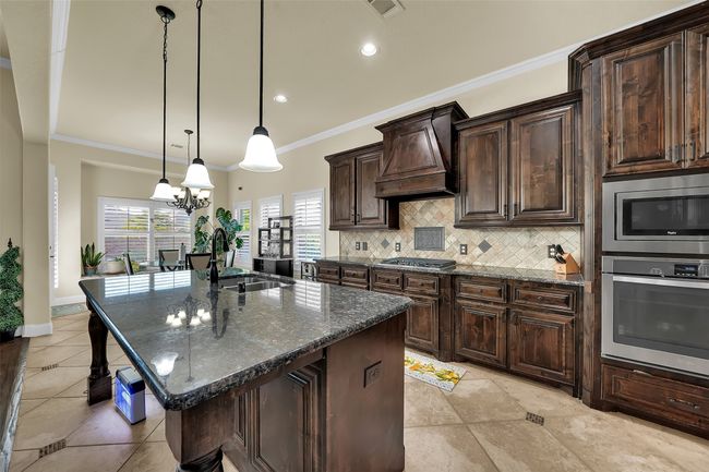 Kitchen featuring dark brown cabinets, crown molding, dark stone countertops, pendant lighting, and stainless steel appliances | Image 8