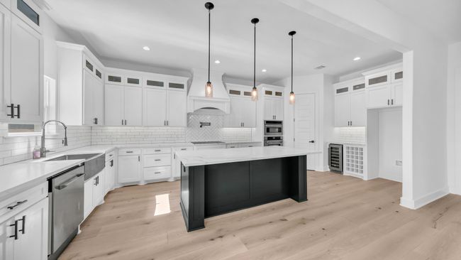 Kitchen with beverage cooler, light wood finished floors, custom exhaust hood, a sink, and stainless steel appliances | Image 14