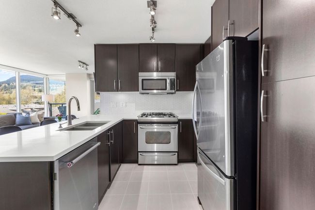 Kitchen featuring stainless steel appliances, light countertops, light tile patterned floors, a sink, and a peninsula | Image 8