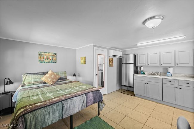 Tiled bedroom with stainless steel refrigerator, an AC wall unit, ornamental molding, and sink | Image 34