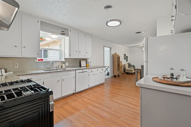 Kitchen with white appliances, light wood finished floors, light countertops, tasteful backsplash, and a textured ceiling | Image 8
