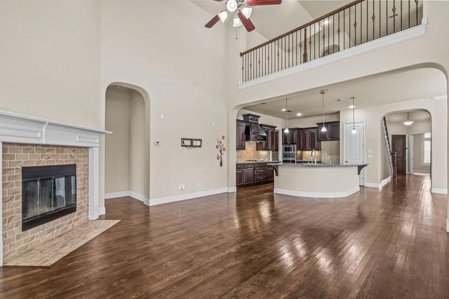 Unfurnished living room featuring a ceiling fan, dark wood-type flooring, a high ceiling, arched walkways, and a fireplace | Image 15