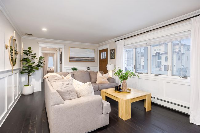 Living room featuring a baseboard radiator, visible vents, crown molding, and dark wood-style flooring | Image 12