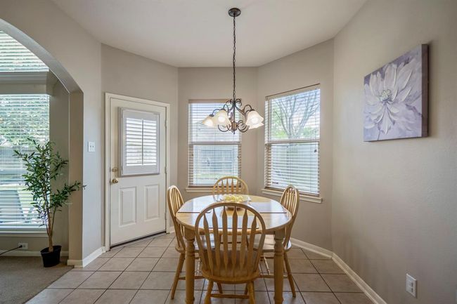 A cozy breakfast nook with bay windows offers a bright space for casual meals, with a door leading out to the back porch. An arched doorway to the left provides a seamless connection back to the living room. | Image 15