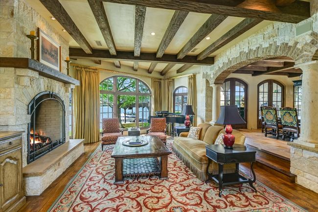 Living room with decorative columns, arched walkways, beam ceiling, hardwood / wood-style flooring, and a stone fireplace | Image 7