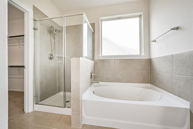 The primary bathroom features a modern design with a glass-enclosed shower, a spacious bathtub, neutral tilework, and a large window providing natural light. | Image 13