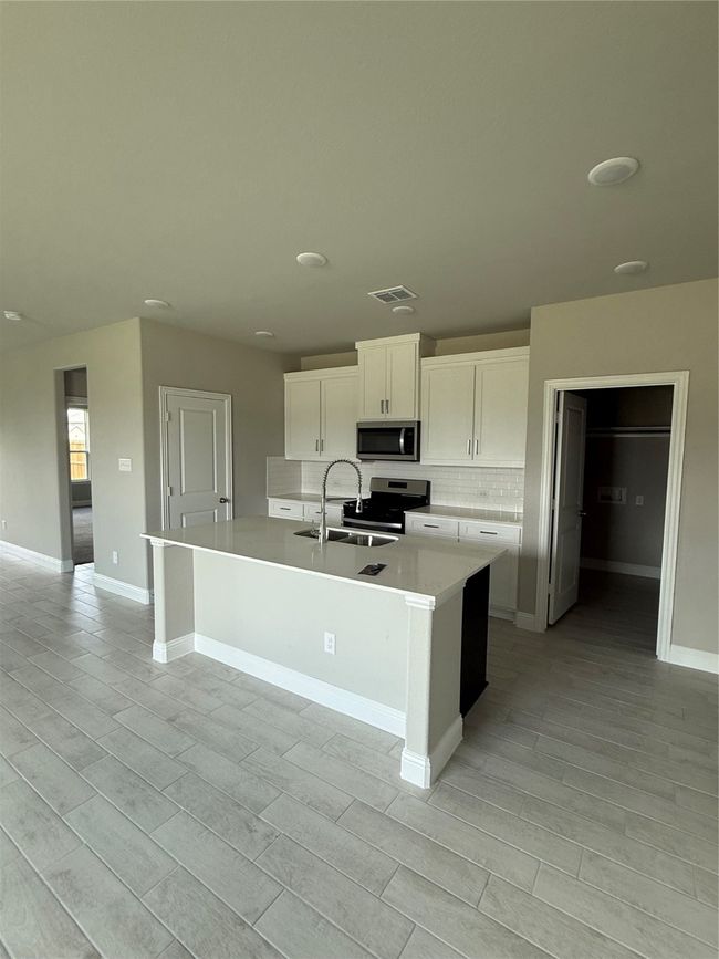 Kitchen with an island with sink, white cabinetry, range, light countertops, and backsplash | Image 6