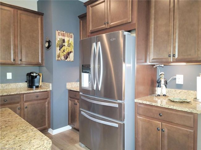Kitchen featuring light wood finished floors, light stone counters, and stainless steel fridge with ice dispenser | Image 13