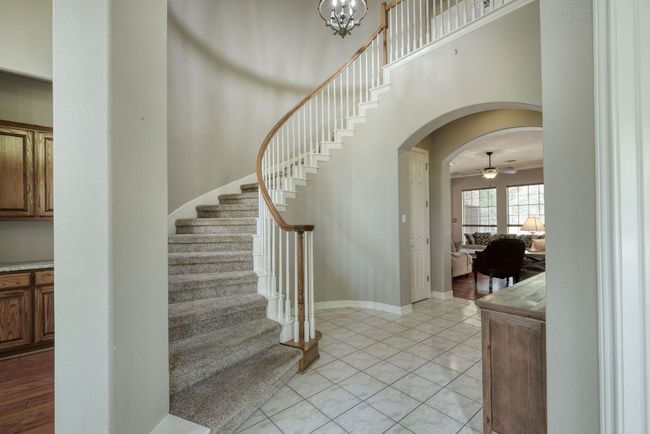 Staircase featuring baseboards, arched walkways, tile patterned floors, and ceiling fan with notable chandelier | Image 7