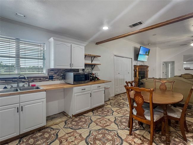 Kitchen featuring stainless steel microwave, ornamental molding, butcher block countertops, decorative backsplash, and white cabinets | Image 16