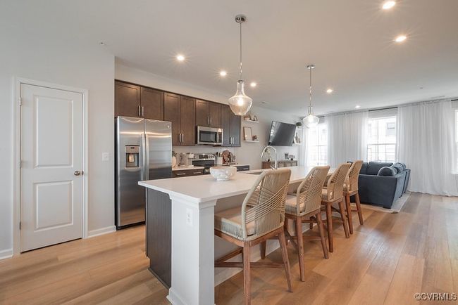 Kitchen with stainless steelappliances, light countertops, a breakfast bar, dark brown cabinetry, and a kitchen island with sink, quartz Countertops | Image 5