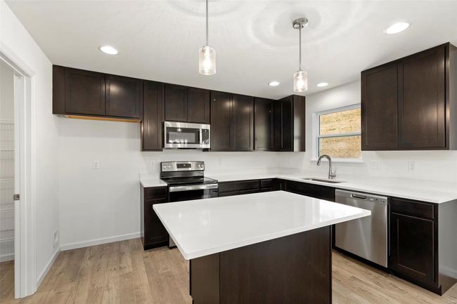 Kitchen featuring light wood-type flooring, pendant lighting, a kitchen island, sink, and appliances with stainless steel finishes | Image 15