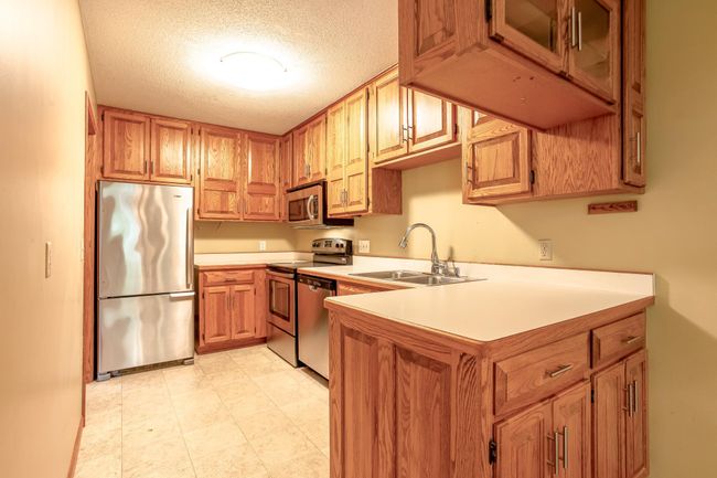 Updated kitchen features abundant oak cabinetry, newer stainless-steel appliances, and laminate tile flooring for easy maintenance. | Image 9