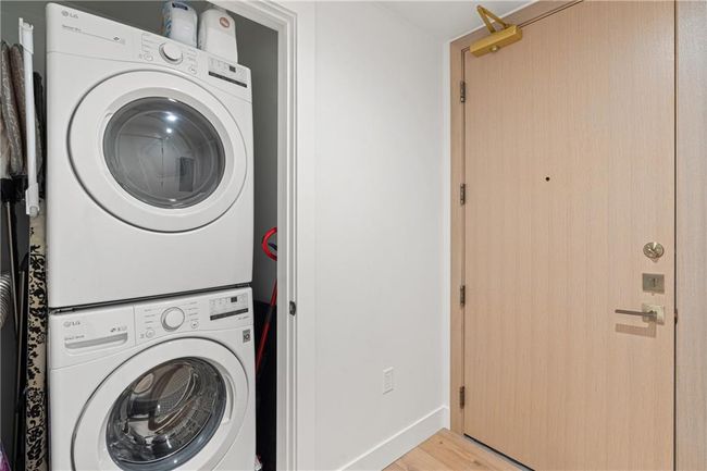 Laundry room with baseboards, light wood-style floors, stacked washer and clothes dryer, and laundry area | Image 22