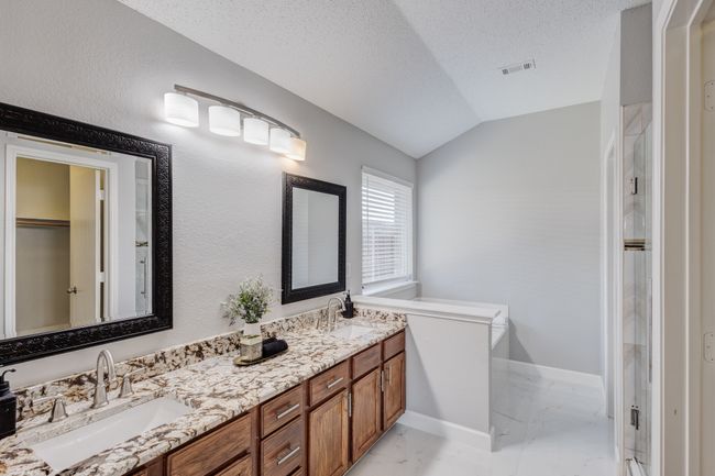 Bathroom with marble look tile flooring, double vanity, lofted ceiling, a textured ceiling, and a shower with shower door | Image 27