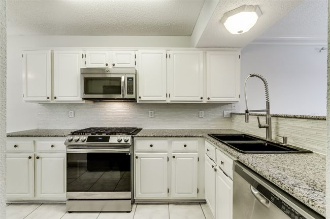 Kitchen featuring white cabinetry, backsplash, stainless steel appliances, and a sink | Image 12
