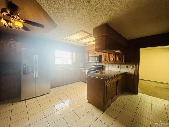 Kitchen featuring ceiling fan, decorative backsplash, appliances with stainless steel finishes, and light tile patterned flooring | Image 6