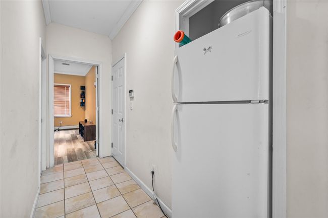 Hallway featuring light tile patterned flooring, baseboards, crown molding, and a baseboard heating unit | Image 38