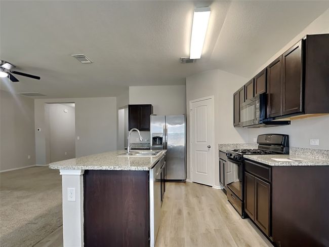 Kitchen with appliances with stainless steel finishes, dark brown cabinetry, an island with sink, and ceiling fan | Image 6