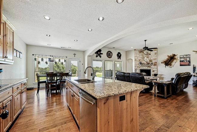 Kitchen featuring stainless steel dishwasher, a ceiling fan, a fireplace, light stone counters, and wood finished floors | Image 12