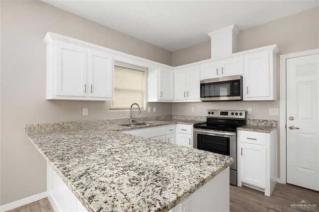 Kitchen with stainless steel appliances, a peninsula, white cabinetry, and light wood finished floors | Image 5