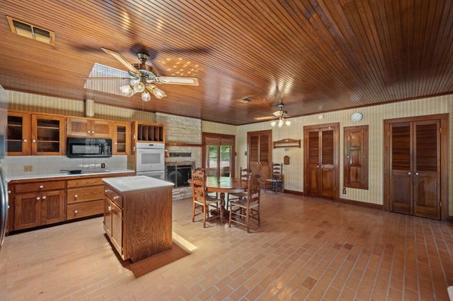 Kitchen featuring microwave, a ceiling fan, a stone fireplace, brick floors, and wood ceiling | Image 12