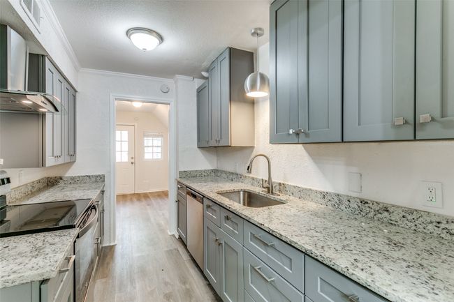 Kitchen with wall chimney exhaust hood, stainless steel appliances, light wood-style flooring, a sink, and crown molding | Image 9