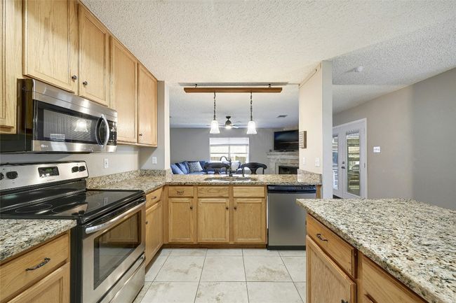 Kitchen with stainless steel appliances, a fireplace, light stone counters, decorative light fixtures, and a textured ceiling | Image 12