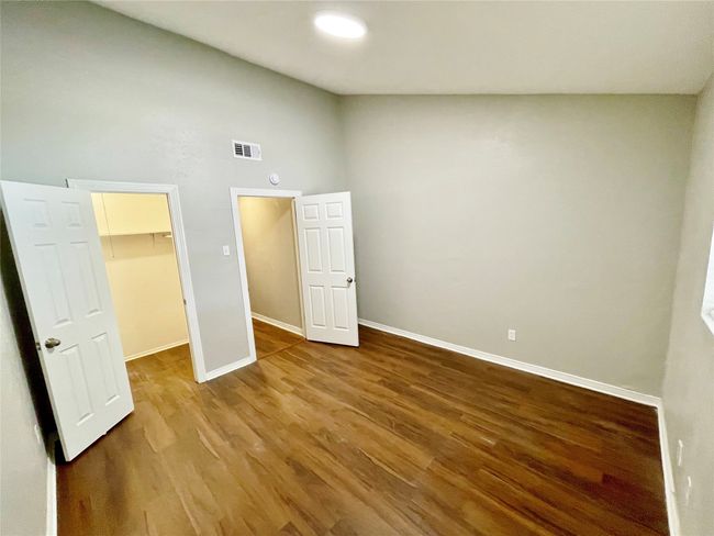 Unfurnished bedroom with a high ceiling, wood finished floors, visible vents, a walk in closet, and baseboards | Image 23